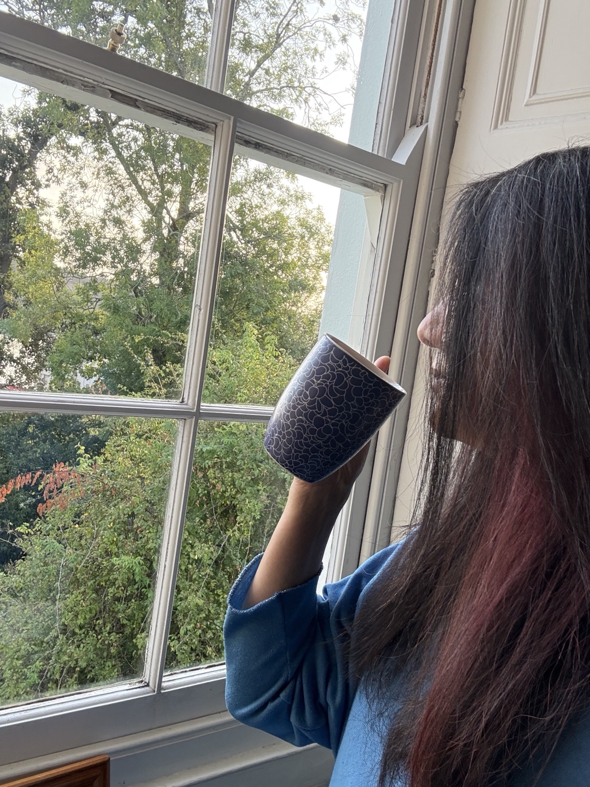 Therese holding a cup of tea and looking out of a window